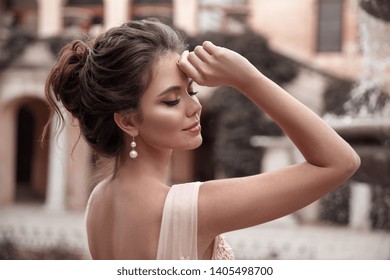 Beautiful bride with pearl earrings jewelry wears pink prom dress. Outdoor romantic portrait  of Attractive brunette woman with makeup and wedding  hair style posing at park. - Shutterstock ID 1405498700