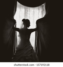 Beautiful bride posing against window. Fine art wedding picture in black and white.