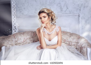 Beautiful bride posing in wedding dress sitting on sofa in a white photo Studio.