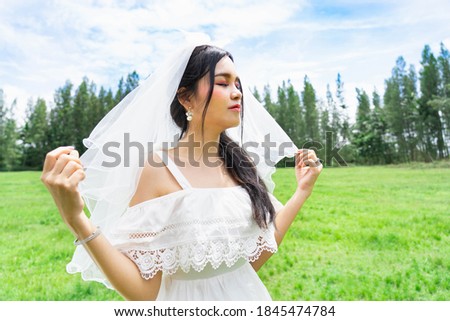 Beautiful bride in white dress and flowing vail in forest location  sunny park on a cloudy day