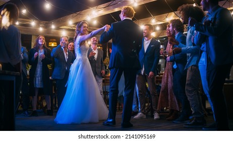 Beautiful Bride in White Dress and Groom in Stylish Black Suit Celebrate Wedding at an Evening Reception Party. Newlyweds Dancing at a Venue with Best Multiethnic Diverse Friends. - Powered by Shutterstock