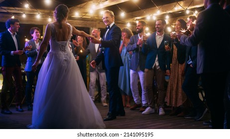 Beautiful Bride in White Dress and Groom in Stylish Black Suit Celebrate Wedding at an Evening Reception Party. Newlyweds Dancing at a Venue with Best Multiethnic Diverse Friends. - Powered by Shutterstock