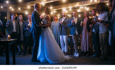 Beautiful Bride in White Dress and Groom in Stylish Black Suit Celebrate Wedding at an Evening Reception Party. Newlyweds Dancing at a Venue with Best Multiethnic Diverse Friends. - Powered by Shutterstock