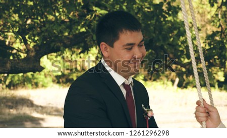 beautiful bride in white dress and groom in red tie, swinging on swing in park in summer. close-up. swing on branch of an oak forest.