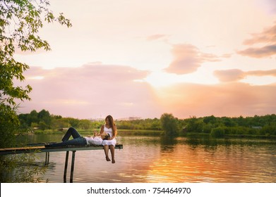 
Beautiful bright fairy walk of a loving couple in the summer at sunset. A guy in a white shirt and jeans with a girl in a sarafan embraces, dancing, sitting on the pier. Pond in the background. Place - Powered by Shutterstock