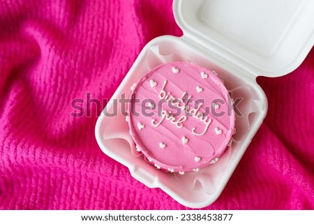 Beautiful bright pink bento cake with an inscription on a pink background. Selective focus, noise. The inscription on the cake Birthday girl 