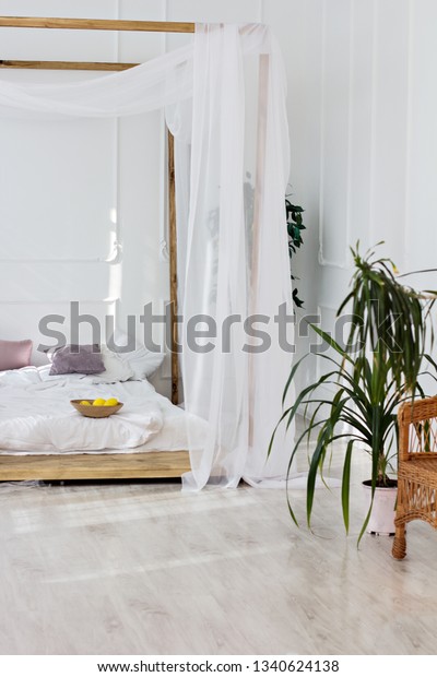 Beautiful bright room and a four-poster bed.\
Cozy bedroom in light colors with a wooden floor, a large\
four-poster bed and basket of flowers. Scandinavian simplicity\
design. Eco loft\
apartments.