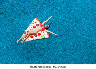 A Beautiful Bright Sexy Funny Woman Is Floating On An Inflatable Pizza In The Pool, Sunbathing, Laughing. Relax On A Tropical Island In The Hotel. Perfect Body And Healthy Skin, Hair, View From Above