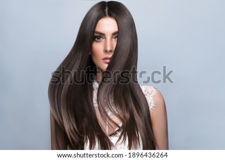 Beautiful brown-haired girl with a perfectly smooth hair, and classic make-up. Beauty face and hair. Picture taken in the studio.
