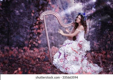 Beautiful Brown-haired Woman With A Flower Wreath On Her Head, Wearing A White Dress Playing The Harp In The Forest
