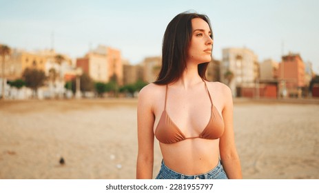 Beautiful brown-haired woman with long hair walks along the beach. Gorgeous girl in swimsuit and denim shorts is walking along the beach. - Powered by Shutterstock