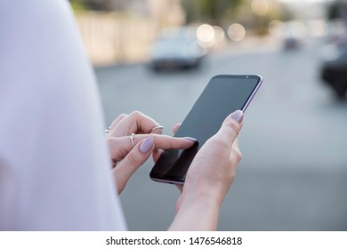 Beautiful Brunette Business Woman In White Skirt And Grey Suit Trousers Working On A Mobile Phone In Her Hands Outdoors. European City On Background. Copy Space.