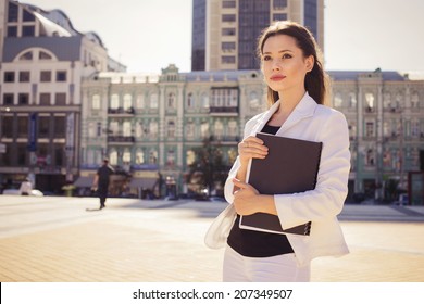 Beautiful brunette business woman in white suit with folder of documents in her hands outdoors. copy space