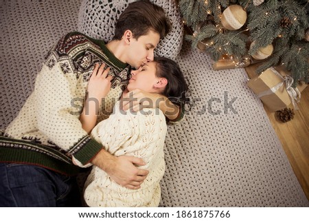 Beautiful brunette caucasian romantic loving couple in cozy warm sweaters in the cabin on a christmas new years eve, smiling, kissing, having fun with each other. Dim dark night light, toned image