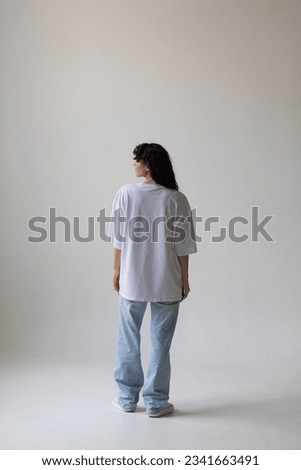 Beautiful brunette with curly hair in a white t-shirt and oversized jeans. Mock-up. Back view.