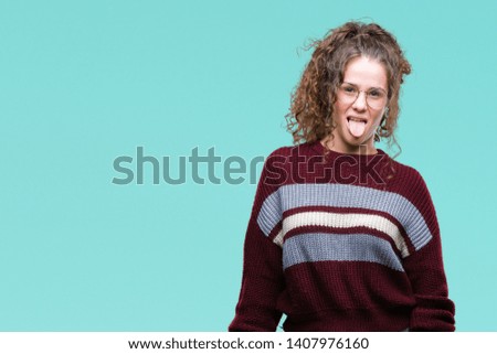 Beautiful brunette curly hair young girl wearing glasses over isolated background sticking tongue out happy with funny expression. Emotion concept.