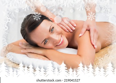 Beautiful brunette enjoying a shoulder massage smiling at camera against fir tree forest and snowflakes