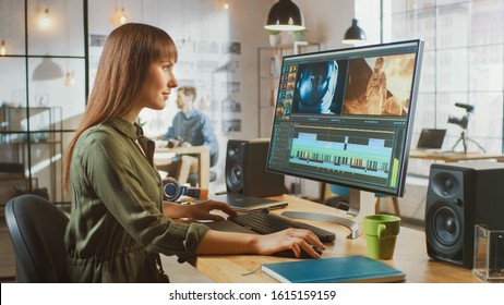 Beautiful Brunette Female Video Editor Works with Footage on Her Personal Computer with Big Display. She Works in a Cool Office Loft. Other Male Creative Colleague Walks in the Background. - Shutterstock ID 1615159159