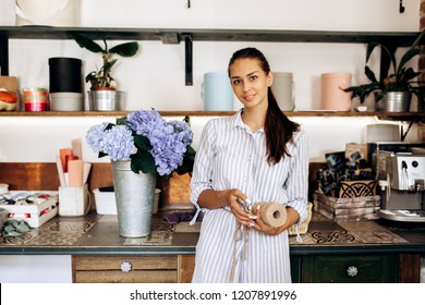 Beautiful brunette girl dressed in a striped dress stands in the flower shop near the vase with light blue hortensia - Powered by Shutterstock