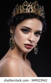Beautiful brunette girl with a golden crown, earrings and professional evening make-up. Beauty face. 