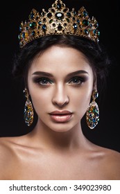 Beautiful brunette girl with a golden crown, earrings and professional evening make-up. Beauty face. 