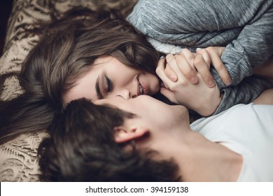 beautiful brunette girl and guy lying in bed and holding tightly hands. The concept of tenderness and affection