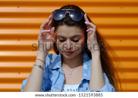 Beautiful brunette girl in jeans and sunglasses on bright orange background in Sunny day