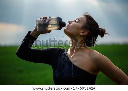 Beautiful brunette girl, with long hair in the wind, drinking from a bottle of water. Outdoors, blue sky background.