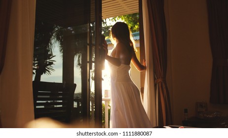 Beautiful brunette girl stands in the doorway in the early morning during sunrise with lens flare effects - Powered by Shutterstock