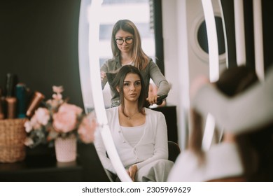 Beautiful brunette girl talking to her hairdresser while she is brushing her hair at the salon - Powered by Shutterstock