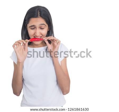 Beautiful brunette girl trying to eat red pepper chilli isolated on white background