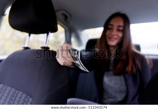 Beautiful brunette giving money for travel sitting\
in taxi