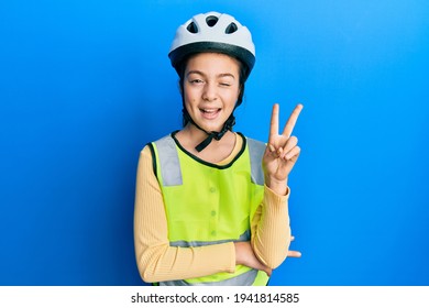 Beautiful brunette little girl wearing bike helmet and reflective vest smiling with happy face winking at the camera doing victory sign. number two. 