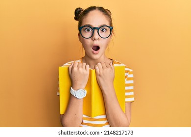 Beautiful brunette little girl wearing glasses and holding book afraid and shocked with surprise and amazed expression, fear and excited face.  - Shutterstock ID 2148217173