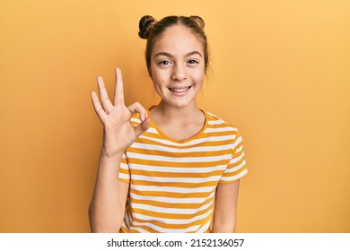Beautiful brunette little girl wearing casual striped t shirt smiling positive doing ok sign with hand and fingers. successful expression. 