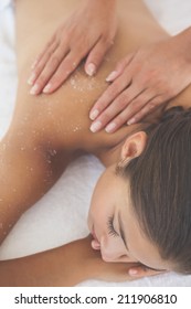 Beautiful brunette lying on massage table with salt scrub on back at the health spa