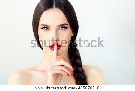 Beautiful  brunette model girl with  long braid hair . Hairstyle  pigtail  . Red lips and nails manicure .Woman  holds a finger on her mouth a secret 