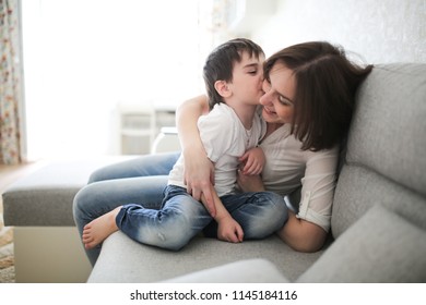 Beautiful Brunette Mom And Son Hugging On Sofa In Real Interior, Soft Focus