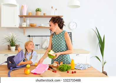 Beautiful Brunette Mother And Her Daughter Packing Healthy Lunch And Preparing School Bag On The Kitchen 