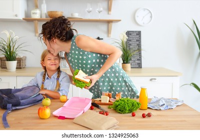 Beautiful Brunette Mother And Her Daughter Packing Healthy Lunch And Preparing School Bag In The Kitchen 