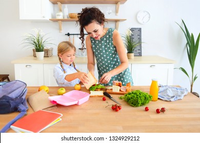 Beautiful brunette mother and her daughter packing healthy lunch and preparing school bag on the kitchen  - Powered by Shutterstock