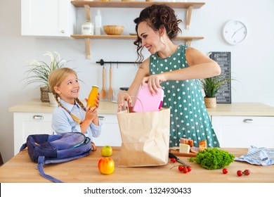 Beautiful Brunette Mother And Her Daughter Packing Healthy Lunch And Preparing School Bag In The Kitchen 