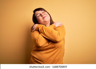 Beautiful brunette plus size woman wearing casual sweater over isolated yellow background Hugging oneself happy and positive, smiling confident. Self love and self care - Powered by Shutterstock