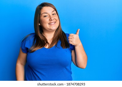 Beautiful Brunette Plus Size Woman Wearing Casual Blue T Shirt Smiling With Happy Face Looking And Pointing To The Side With Thumb Up. 