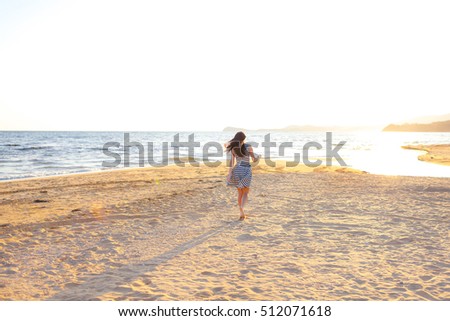 Beautiful brunette in a striped dress. Young woman walking on the beach in the evening.