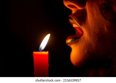 beautiful brunette vampire girl with bloody teeth blows on a candle flame. High quality photo