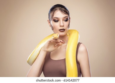 Beautiful brunette woman with a albine python. Fashion makeup, beige background
