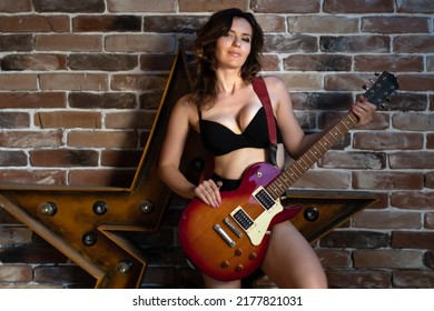 A Beautiful Brunette Woman In Black Lingerie With Big Breasts Stands Near A Brick Wall With An Electric Guitar A Musical Instrument