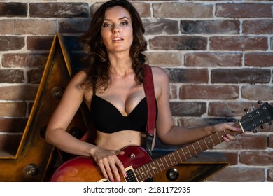 A Beautiful Brunette Woman In Black Lingerie With Big Breasts Stands Near A Brick Wall With An Electric Guitar A Musical Instrument