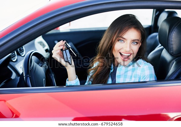 Beautiful brunette woman driving\
red car, purchasing automobile. Happy owner of new car, looking at\
camera, nice smile, holding keys. Head and shoulders, happy\
driver